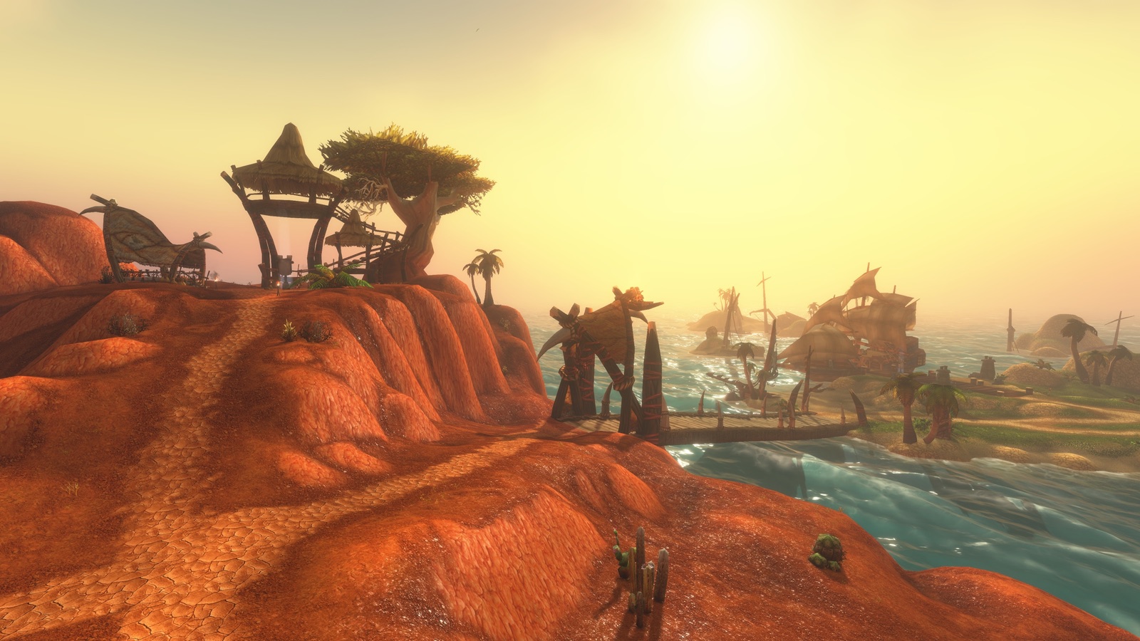 In-game screenshot: a troll hut and twisted tree on a red-rock hill above a turquoise bay, with wrecked ships on the far shore at sunset